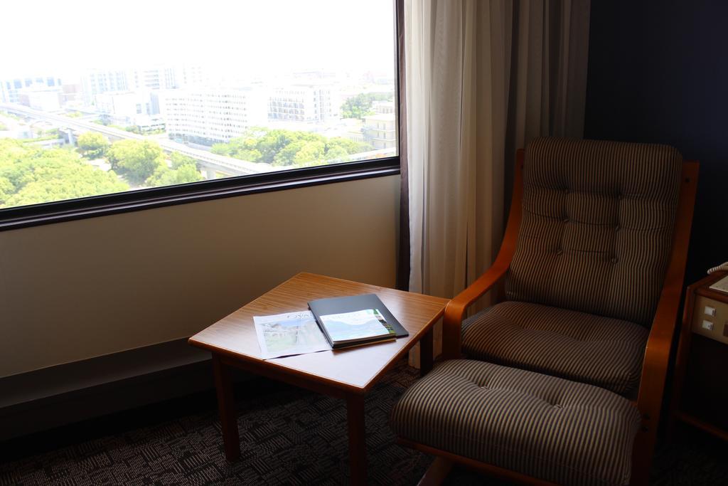 Kobe Portopia Hotel Esterno foto The image depicts a cozy corner of a room featuring a comfortable chair next to a small wooden table. The chair has a cushioned back and seat, and is positioned near a large window that offers a view of the outdoors, which is not fully visible. On th