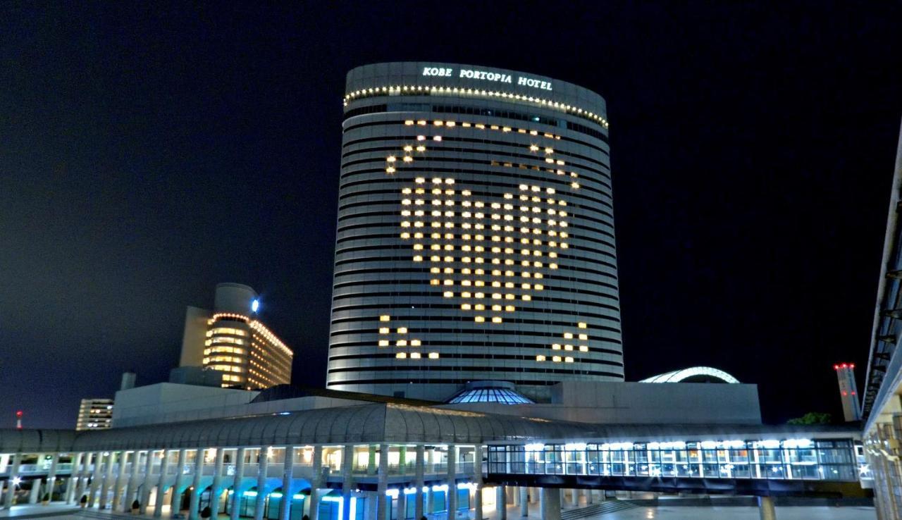 Kobe Portopia Hotel Esterno foto The photo shows a large hotel building at night, with illuminated windows forming a heart shape on its facade. The hotel is labeled as "Kobe Portopia Hotel." In the foreground, there is a structure that appears to be part of the hotel complex, along 